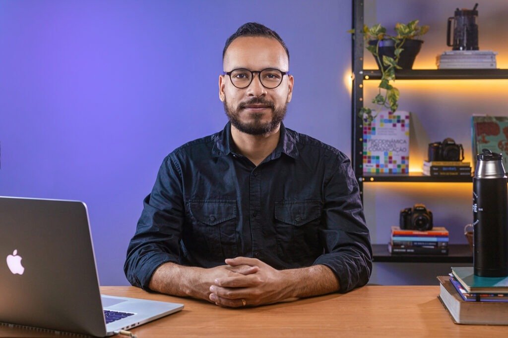Léo Tavares designer sentado em uma mesa com livros e um computador
